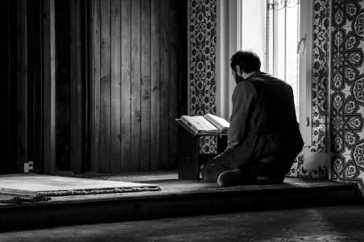 A man reading Quran beside a window